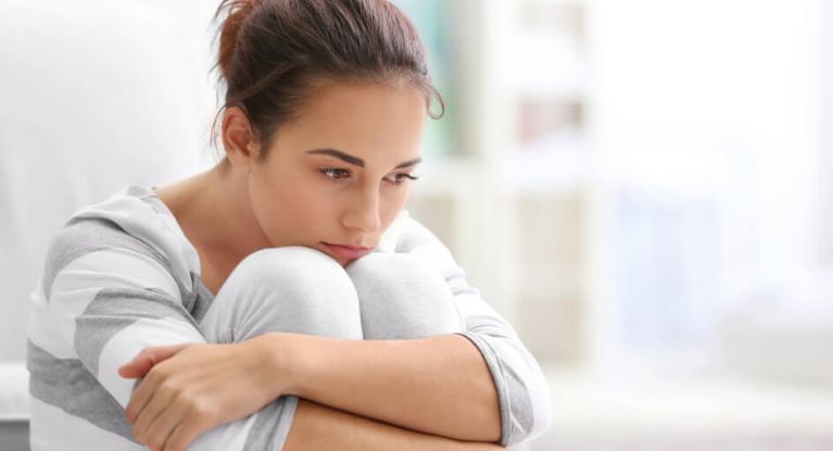 Depressionen – Symptome, Risikofaktoren & Behandlung Frau umschlingt ihre Beine und schaut nachdenklich