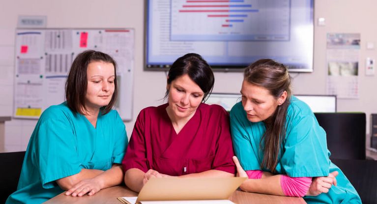 Teambesprechung Drei weibliche Pflegekräfte besprechen die Übergabe