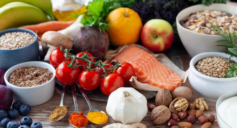 Auf diesem Bild sind viele gesunde Nahrungsmittel zu sehen, darunter Lachs, Tomaten, Kräuter, Nüsse