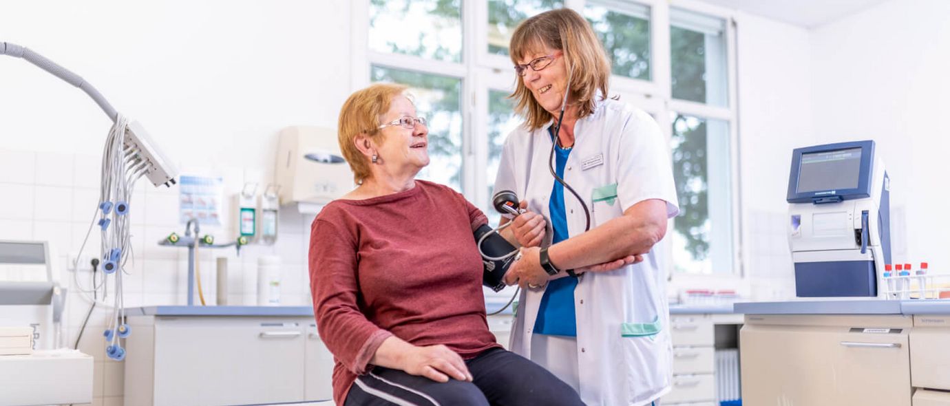 Pflegekraft misst Blutdruck einer älteren Patientin