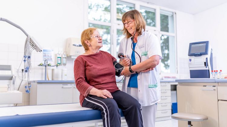 Pflegekraft misst Blutdruck einer älteren Patientin